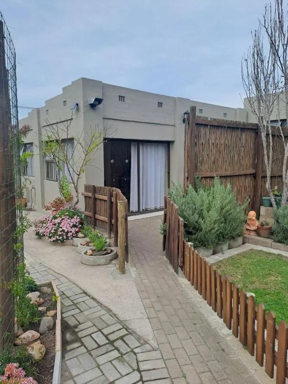 Modern apartment entrance with paved courtyard, wooden fencing, potted plants and flowers