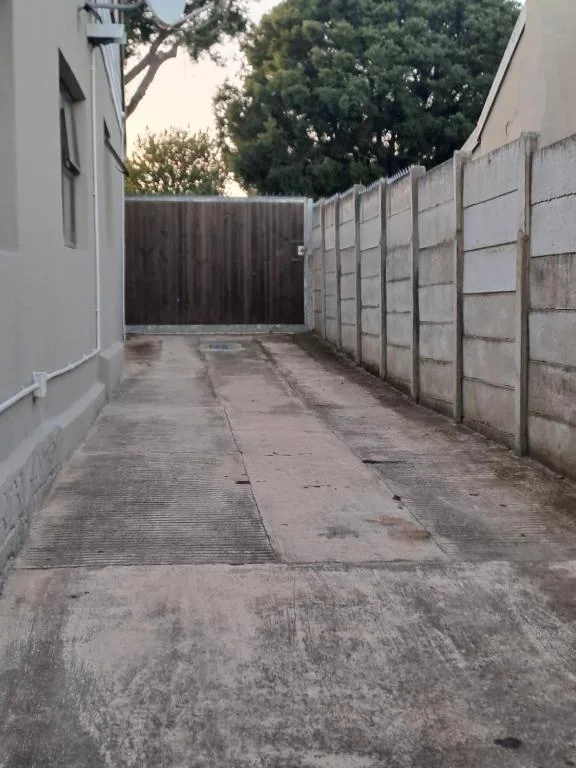 Concrete driveway and fenced parking area with mature trees above
