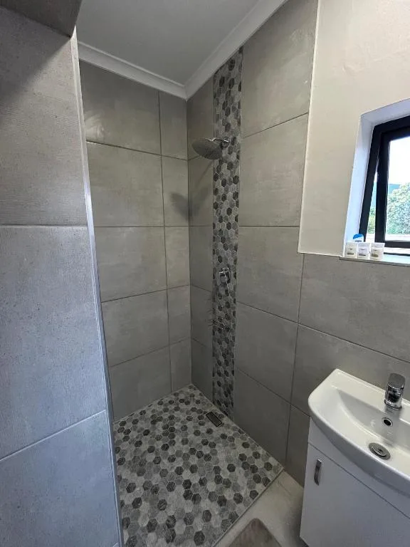 Modern bathroom with walk-in shower, gray tile walls, patterned floor, and white sink