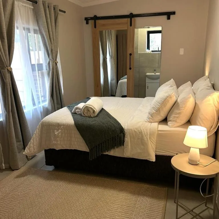 Bright bedroom with neatly made bed, multiple pillows, and ensuite bathroom visible through sliding barn door