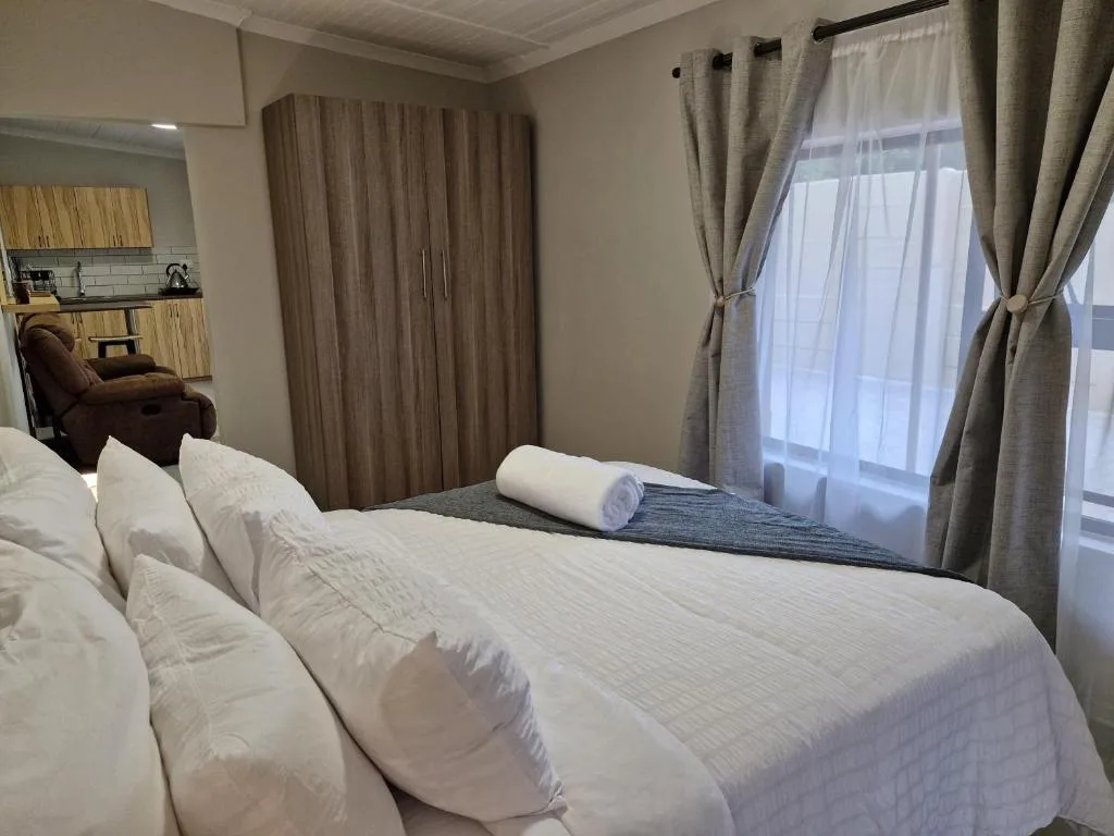 Spacious bedroom with white bedding, wooden wardrobe, and large windows