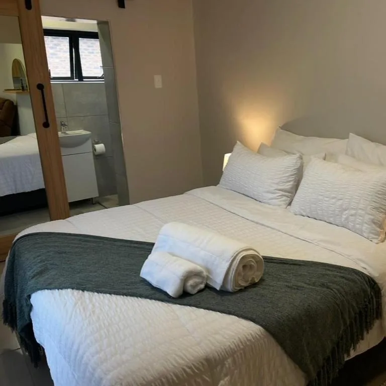 Modern bedroom with white pillows, rolled towels, and ensuite bathroom visible through door