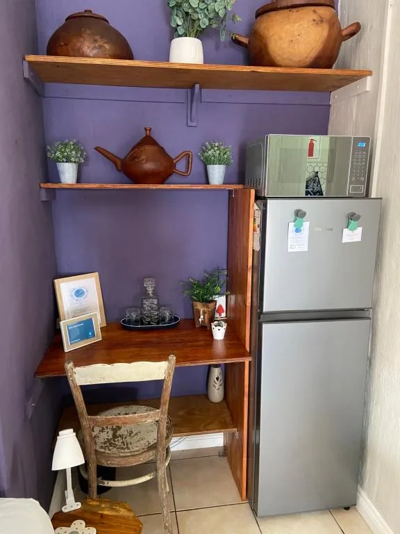 Compact kitchen nook with wooden shelving, refrigerator, and decorative pottery