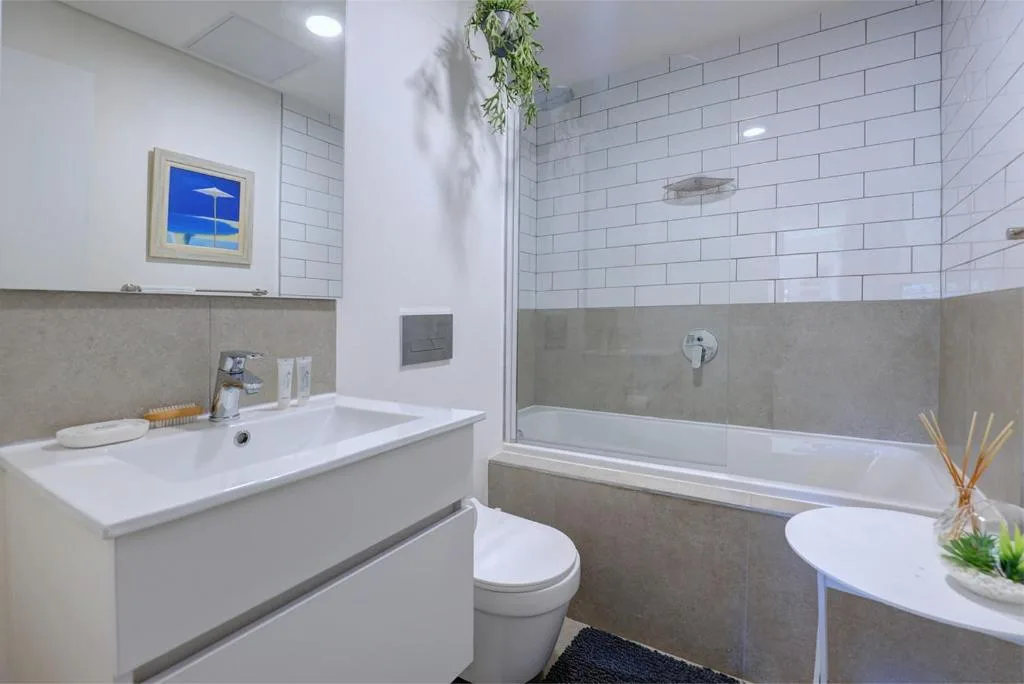 Modern bathroom with white subway tiles, vanity sink, toilet, and bathtub with shower enclosure
