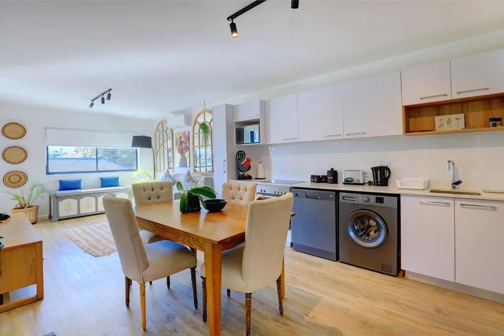 Modern open-plan kitchen with white cabinetry, black appliances, and wooden dining table