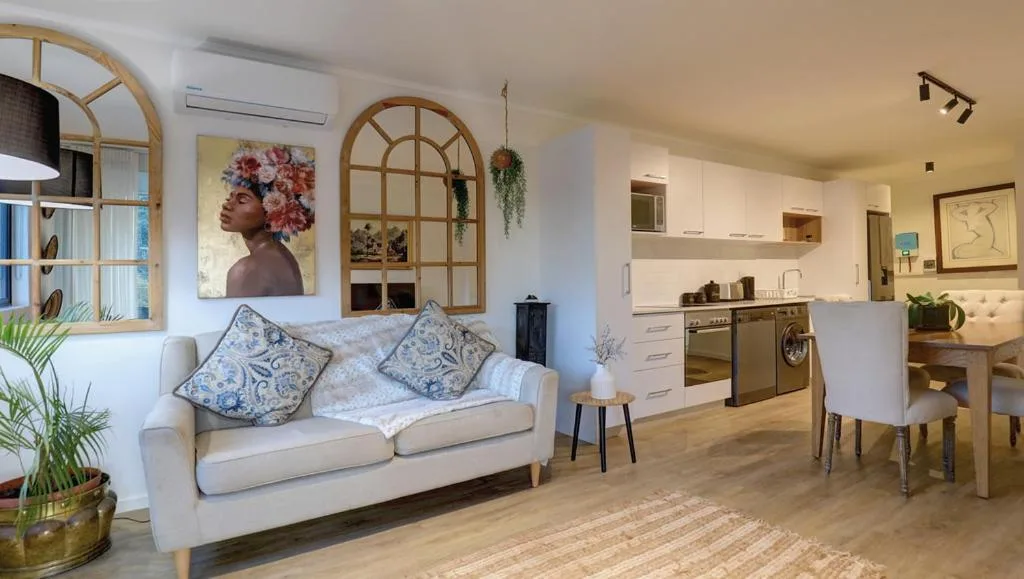 Bright open-plan lounge with cream sofa, decorative pillows, and modern kitchen visible