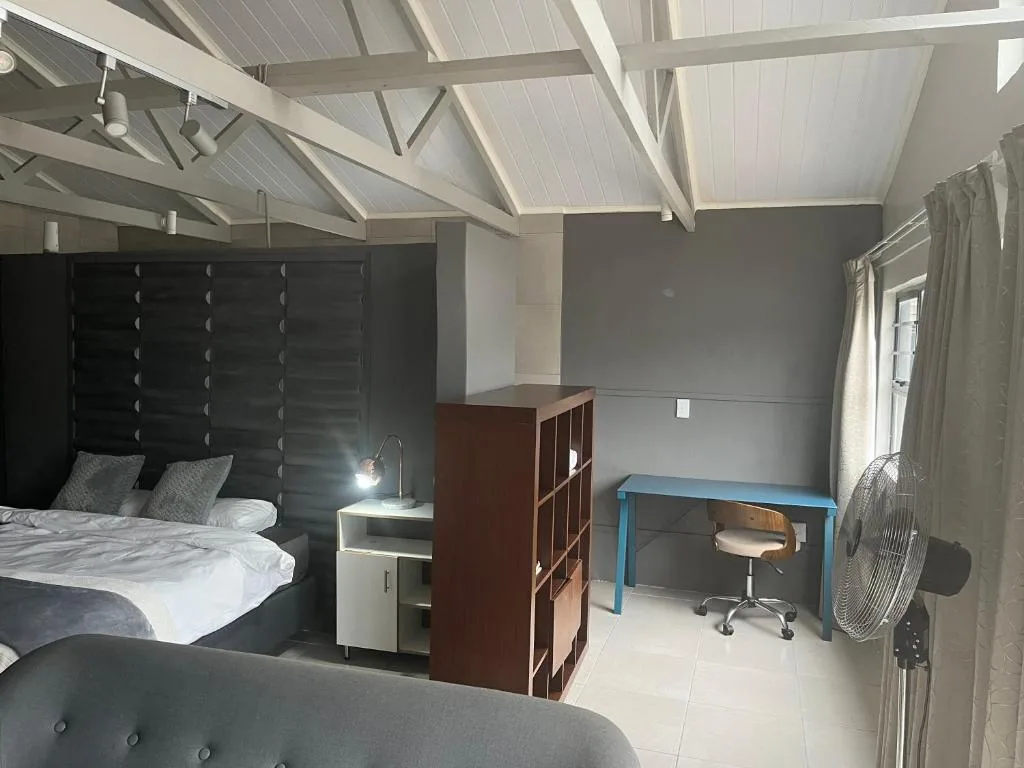 Modern bedroom with black headboard, white bedding, desk workspace, and vaulted ceiling