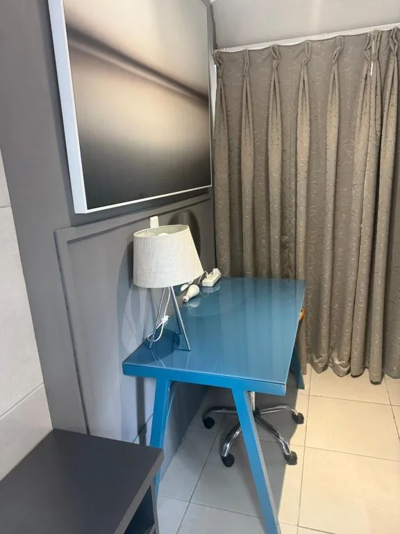 Bright bedroom with flat-screen TV, blue desk, and table lamp