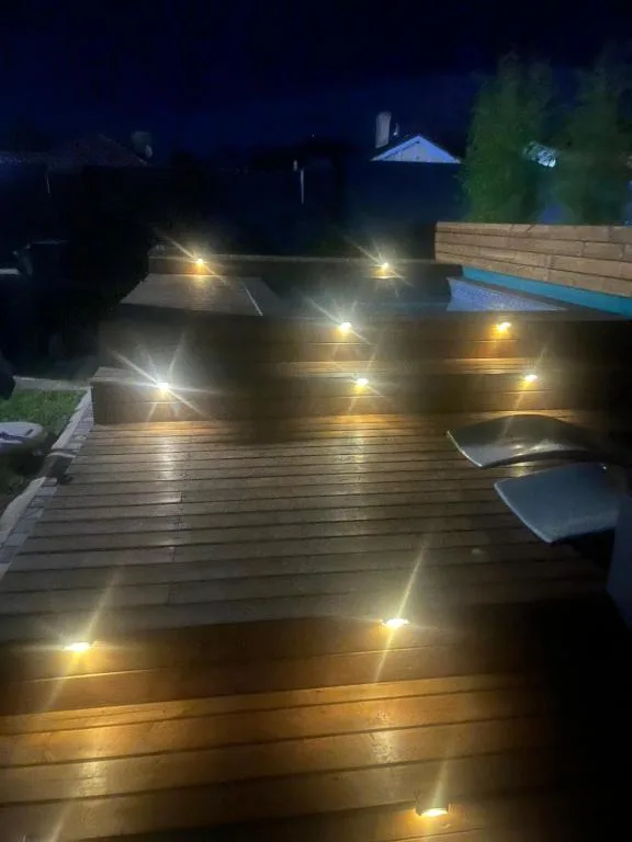 Illuminated wooden deck at night with ambient lighting and lounge chairs