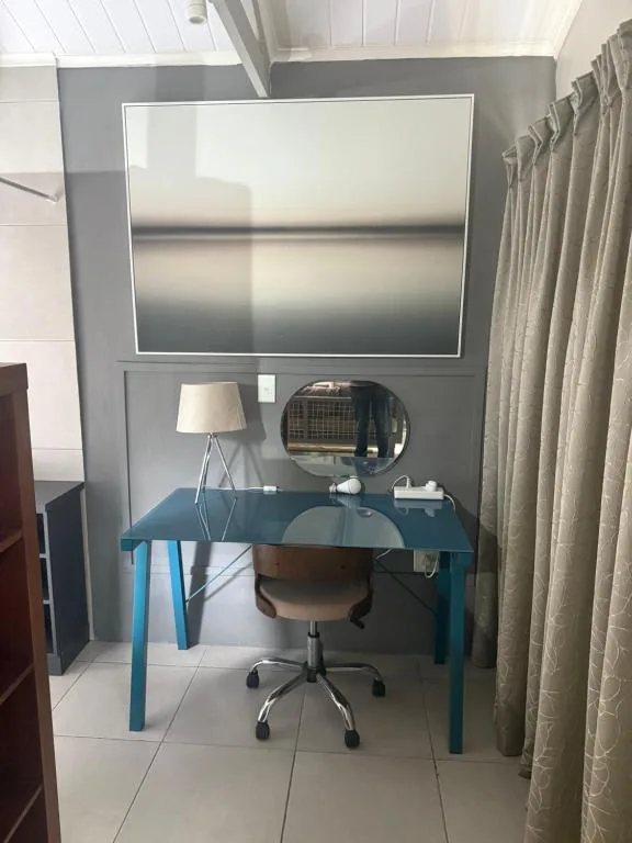 Modern workspace with blue glass desk, wall-mounted TV, and desk lamp
