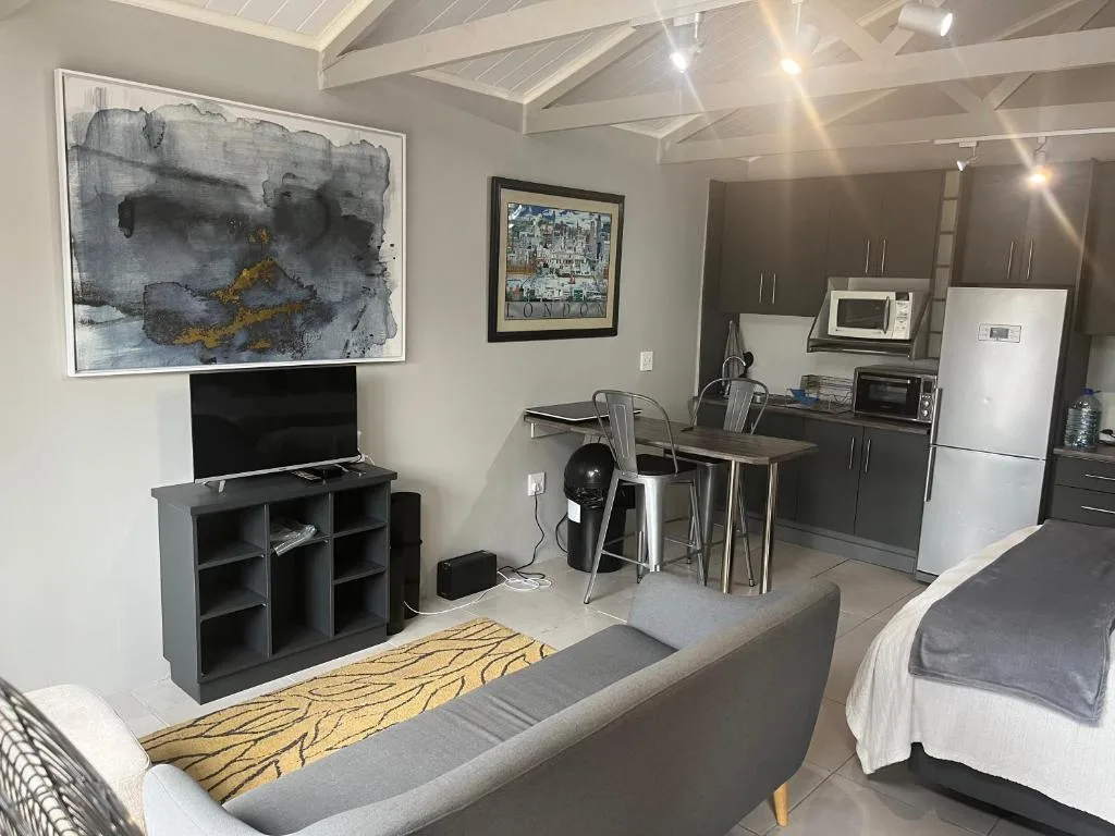 Open-plan studio with gray sofa, TV, and kitchenette visible in background