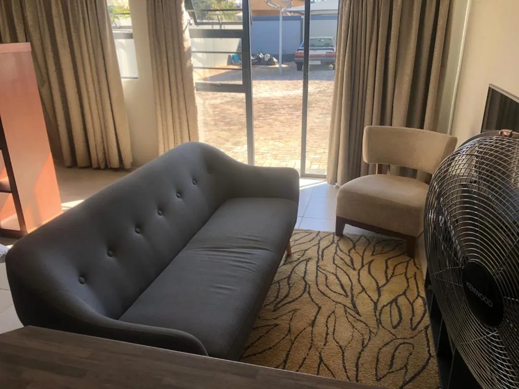 Modern living room with black sofa, neutral chair, patterned rug, and glass doors