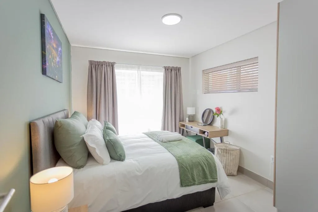 Modern bedroom with queen bed, soft green accents, and natural light from large windows