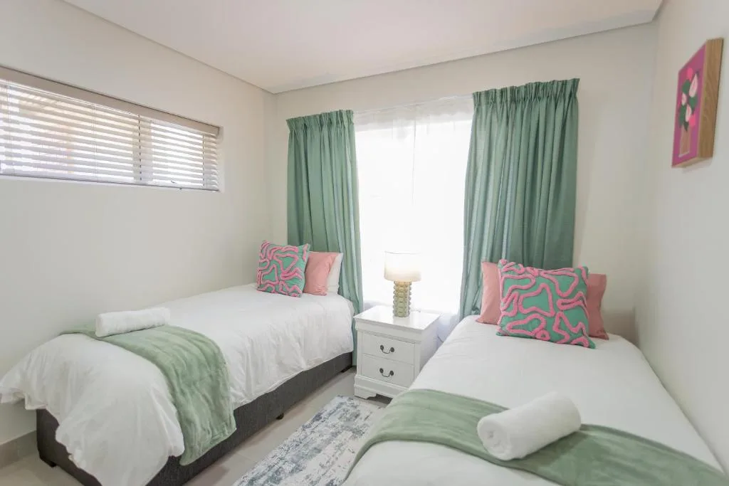 Twin bedroom with white beds, colorful cushions, and green curtains