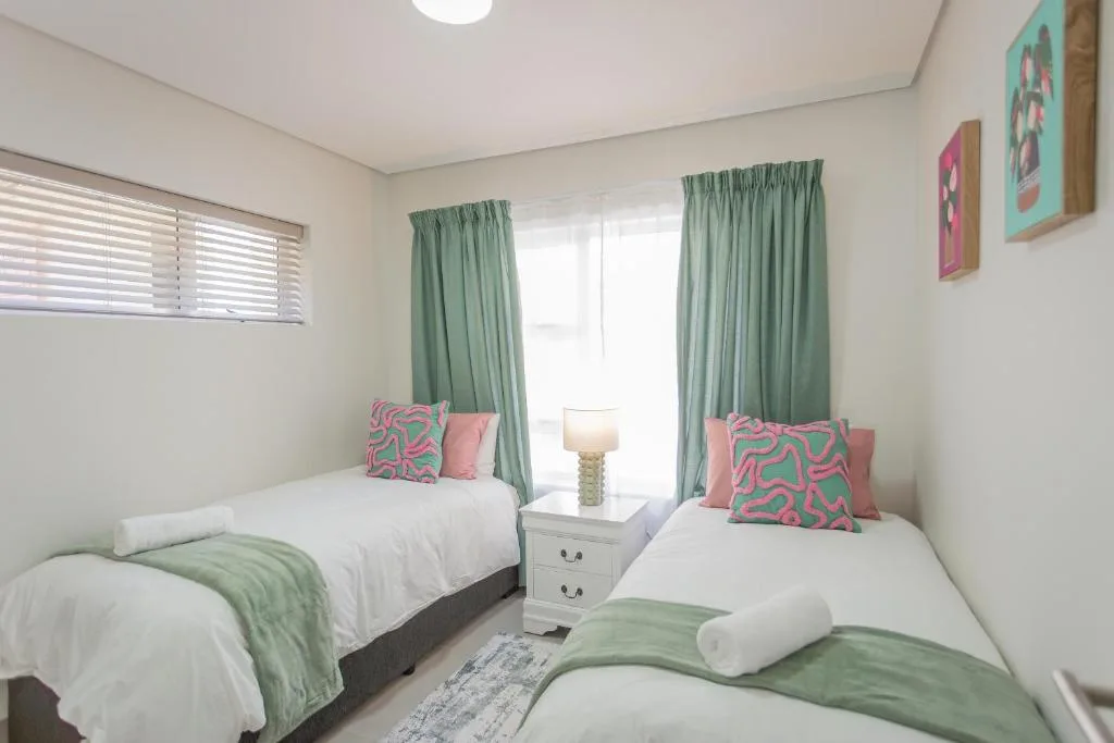 Twin bedroom with white beds, colorful cushions, green curtains, and modern decor