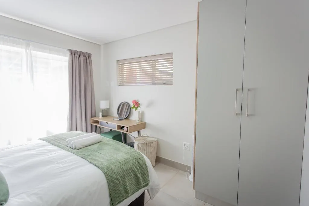 Bright bedroom with white bedding, green throw, and modern wooden vanity desk