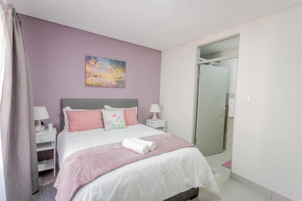 Bright bedroom with purple accent wall, queen bed, pink linens, and ensuite bathroom access