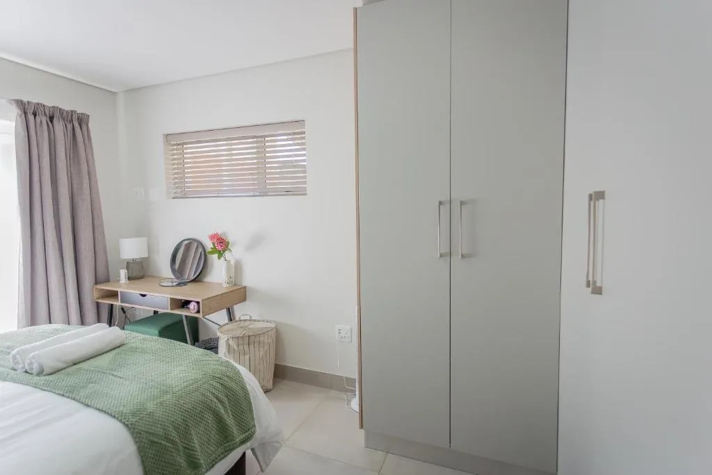 Bright bedroom with green bedding, vanity desk, and modern fitted wardrobe