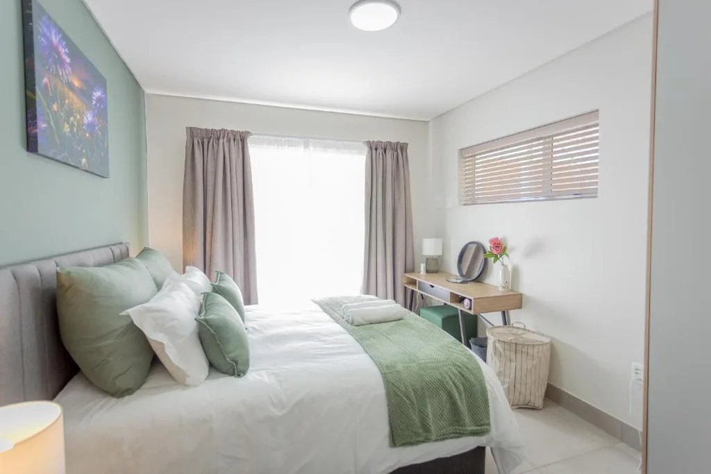 Bright bedroom with queen bed, green accents, vanity desk and garden views