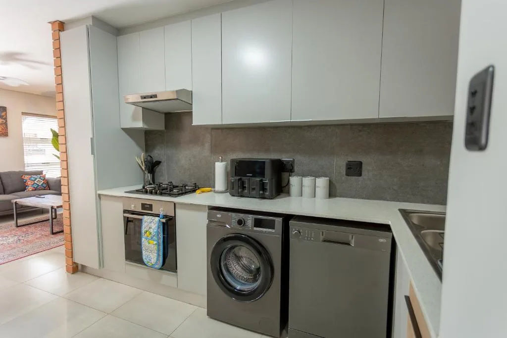 Modern kitchen with white cabinetry, gas cooktop, washing machine, and grey backsplash