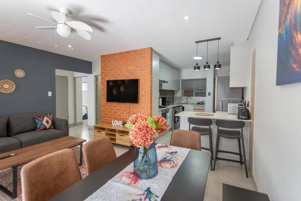 Open-plan lounge with dining area, orange brick feature wall, and kitchen access