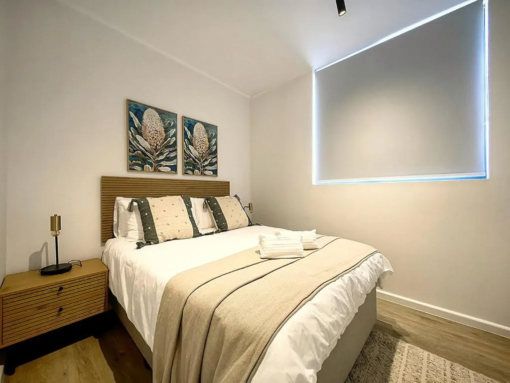 Modern bedroom with neatly made bed, wooden headboard, and botanical wall art