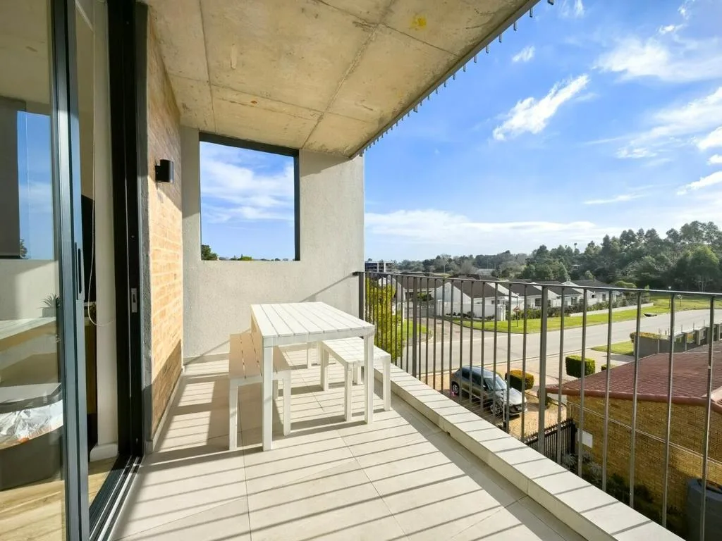Spacious modern balcony with white furniture overlooking residential area and trees