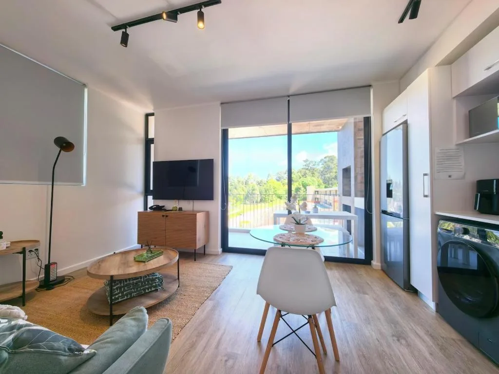 Modern lounge with sofa, TV, and glass dining table overlooking deck
