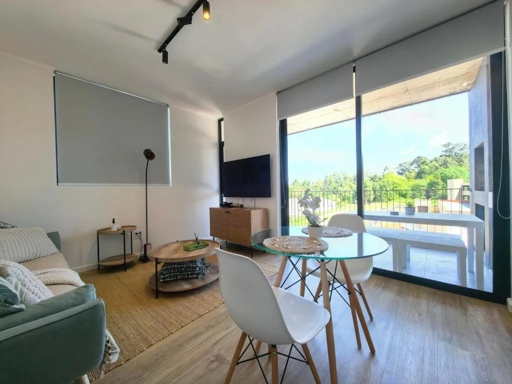 Modern lounge with sofa, TV, dining table, and garden views through sliding doors