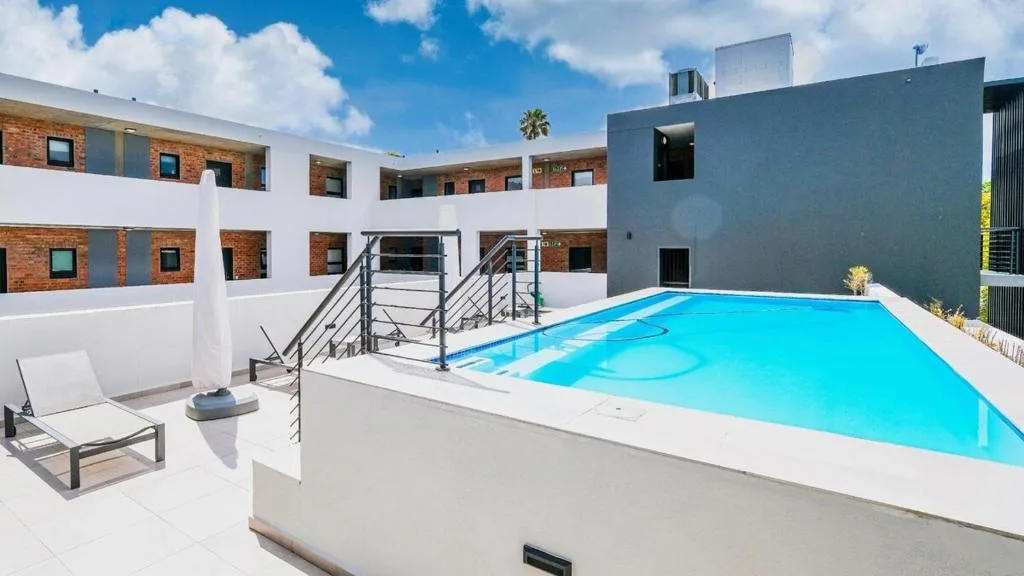 Bright turquoise swimming pool with lounger and modern apartment building