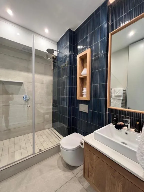 Modern bathroom with black tiled shower, white vanity, wooden accents, and recessed lighting