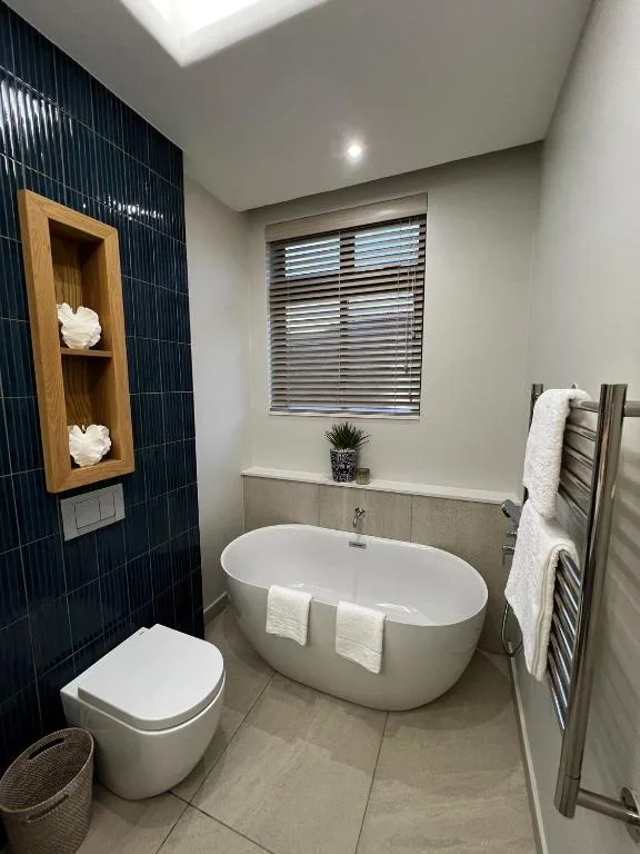 Modern bathroom with freestanding bathtub, dark tile accent wall, and skylight