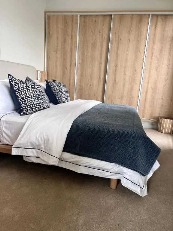 Modern bedroom with neatly made bed, patterned pillows, and wooden wardrobe