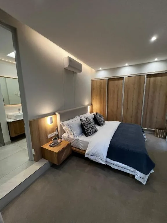 Modern bedroom with queen bed, wooden nightstand, and ensuite bathroom visible