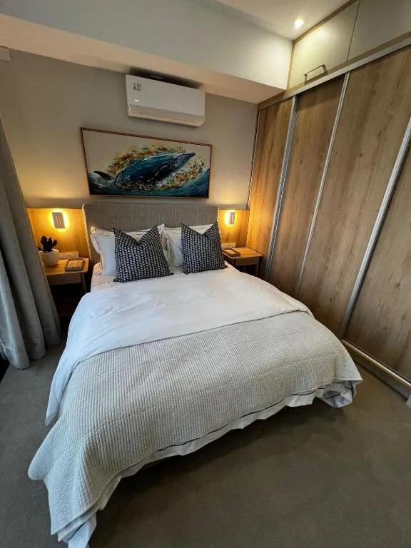 Modern bedroom with queen bed, warm lighting, and ocean artwork above headboard