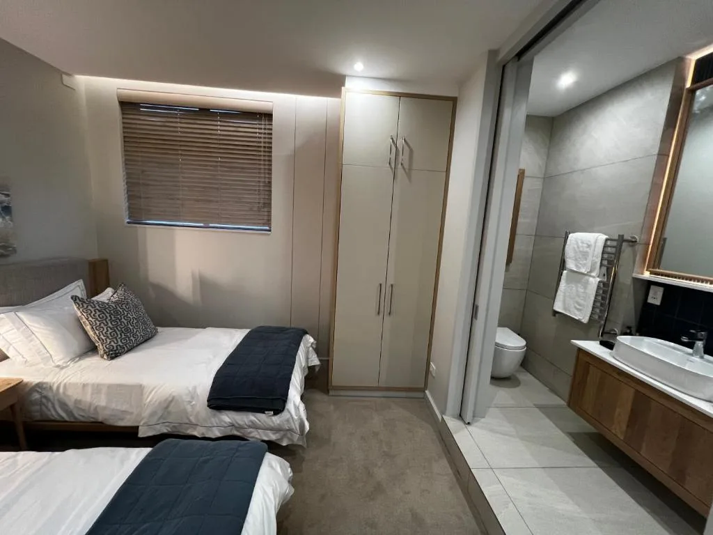 Modern bedroom with two beds, wardrobe storage, and ensuite bathroom visible