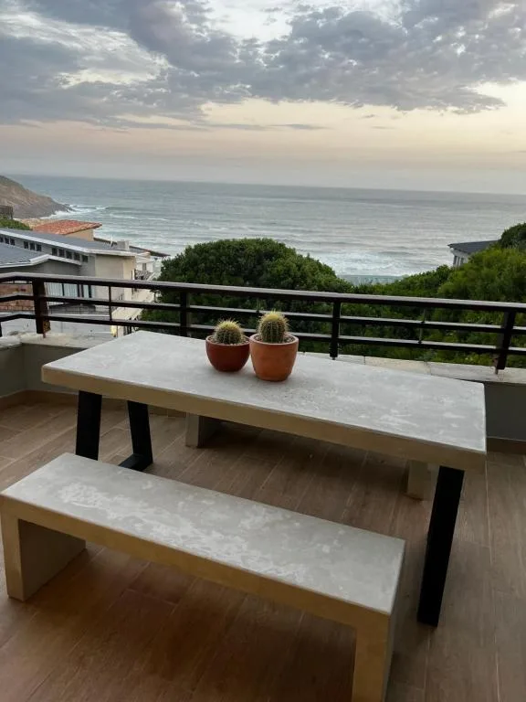Ocean view deck with dining table, cacti, and coastal scenery at sunset