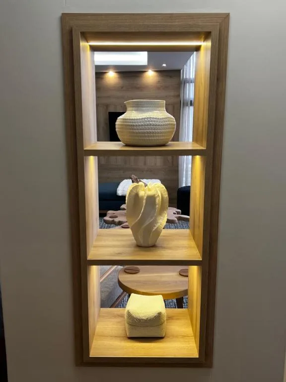 Wooden wall-mounted display shelf with three lit compartments showcasing decorative ceramic vessels