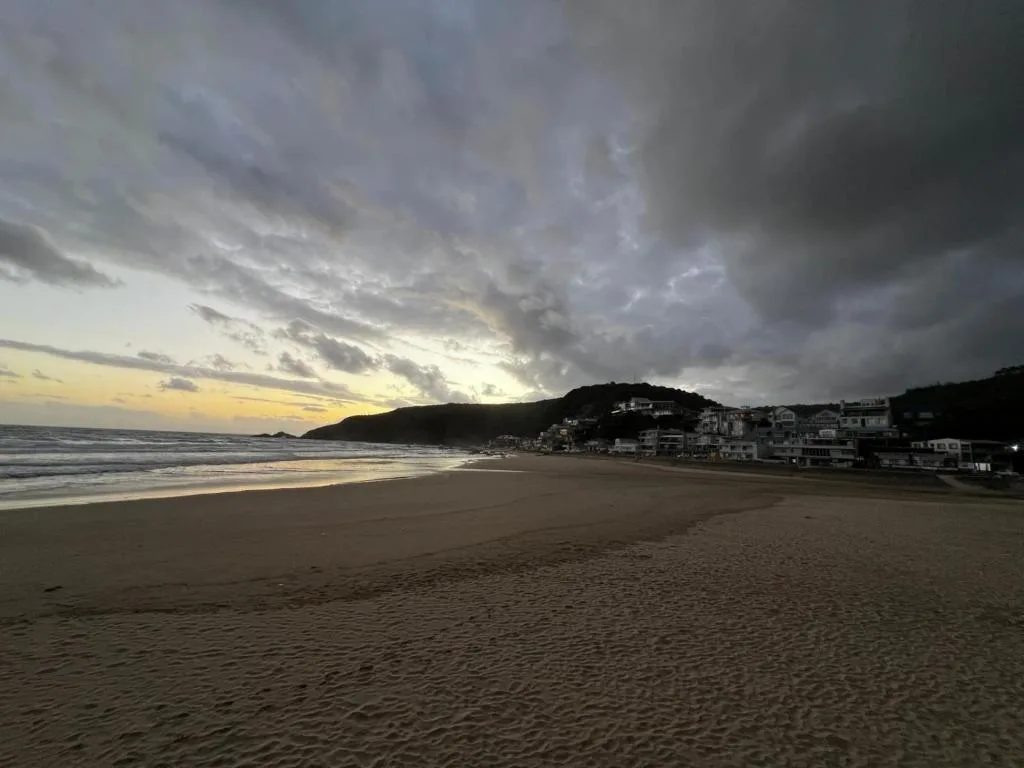 Sunset beach view with coastal town nestled against forested headland