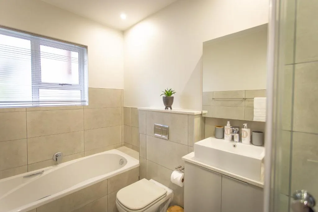 Modern bathroom with beige tiling, bathtub, toilet, and white vanity sink