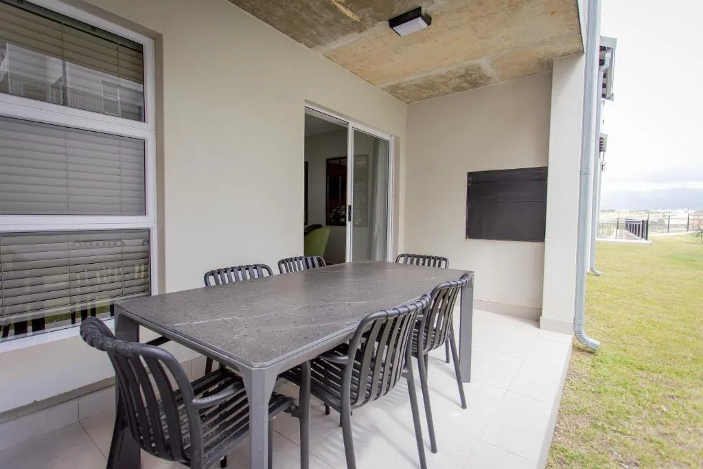 Covered outdoor patio with dining table and chairs overlooking green lawn