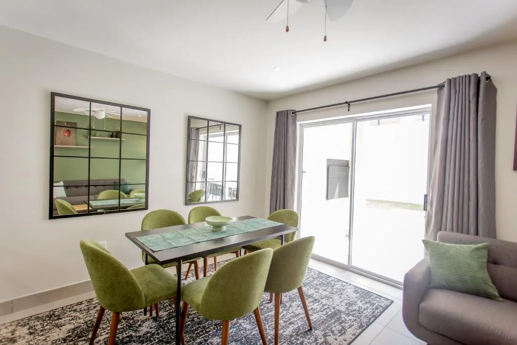Modern dining area with green chairs and table, opening to deck