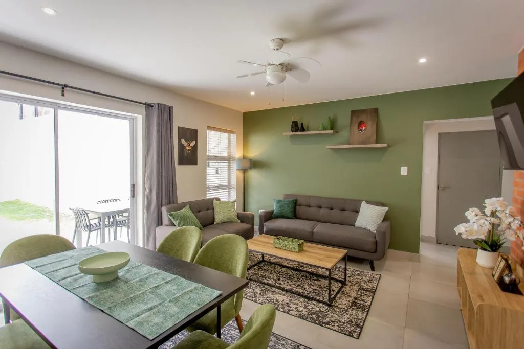 Modern lounge with gray sofa, green accent wall, and open-plan dining area