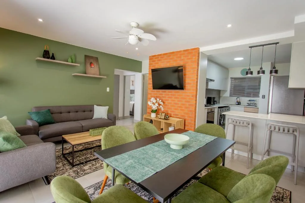 Modern open-plan lounge with green accent wall, brown sofa, and dining area