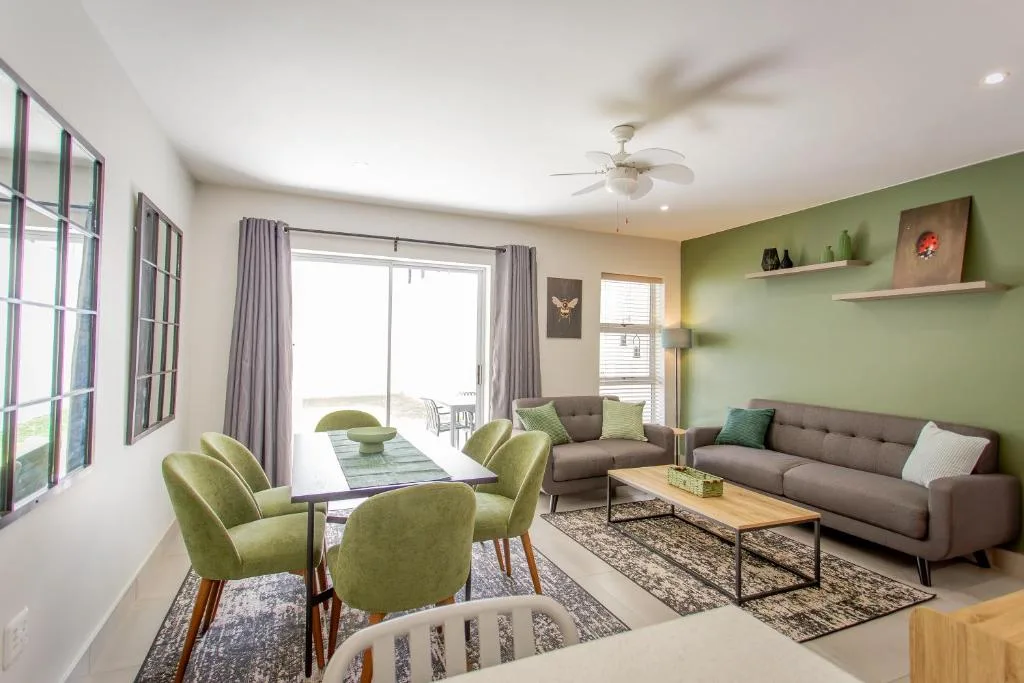 Modern lounge with gray sofa, green armchairs, and dining area overlooking deck
