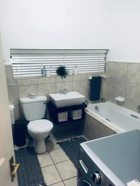 Modern bathroom with toilet, sink vanity, bathtub, and tiled walls