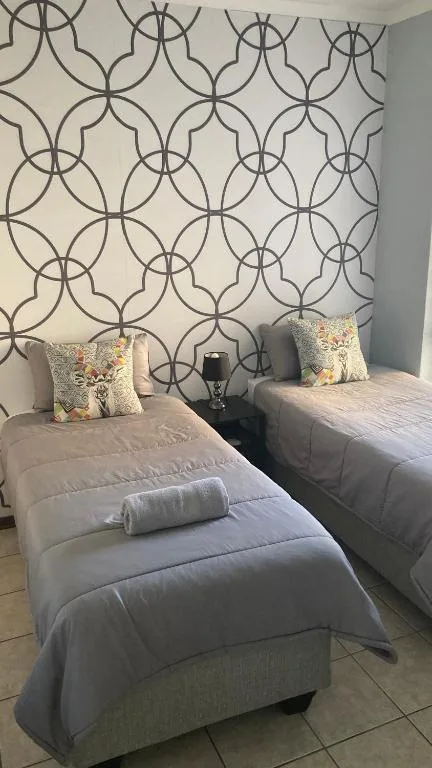 Twin beds with grey linens and decorative pillows against patterned accent wall
