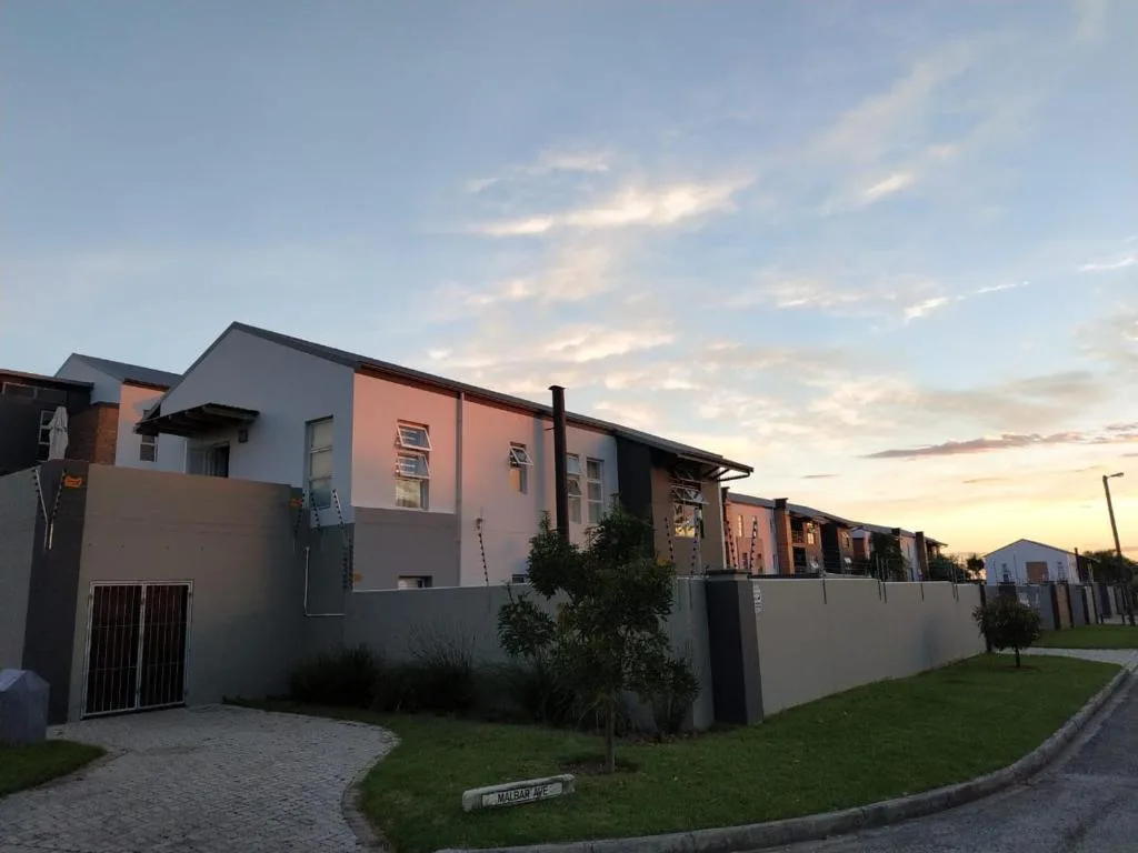 Modern townhouse facade at sunset with paved driveway and landscaped garden