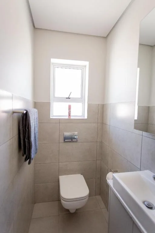 Clean bathroom with wall-mounted toilet, sink, and natural window light