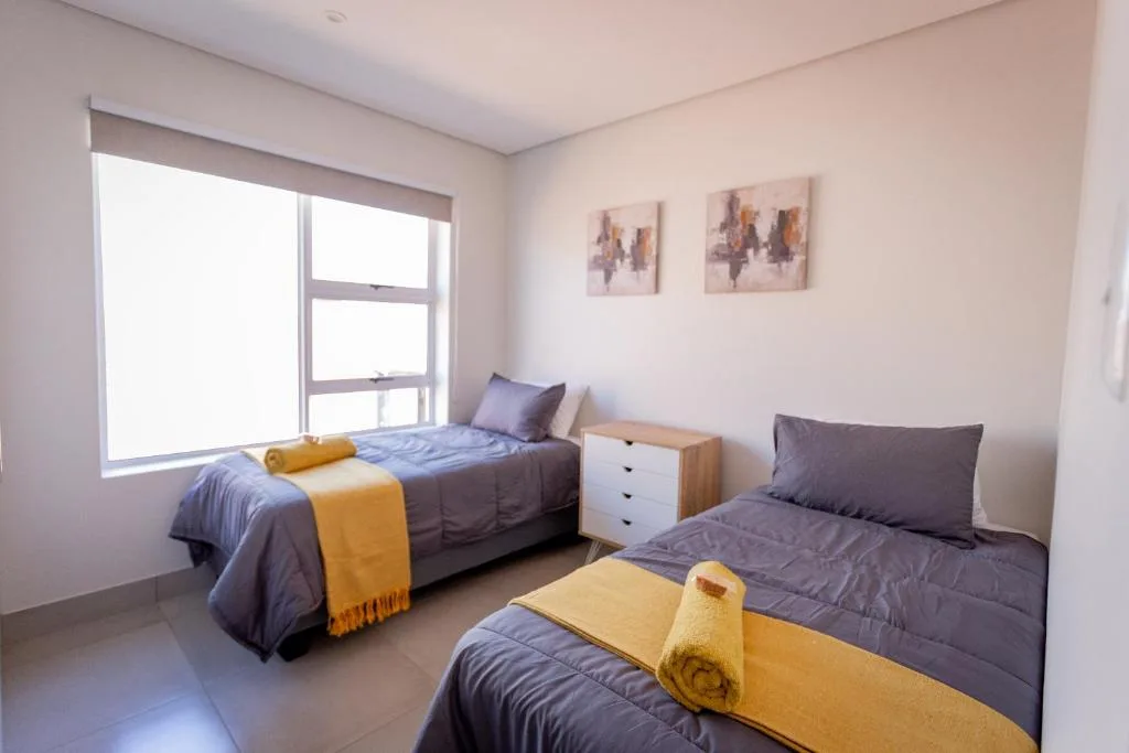 Twin bedroom with two single beds, yellow accents, and large window